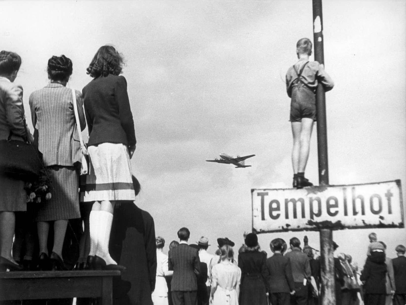 1948 年,柏林市民在坦佩爾霍夫機場外看著一架空運飛機降落。